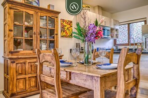 A dining area with a wooden table set for four, surrounded by chairs. A cabinet with glass doors is to the left.