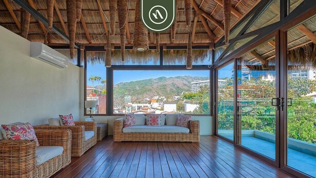 A room with a wicker sofa, a glass door leading outside, and a view of a mountain. - 1 BR Condo in Romantic Zone - Amazing Rooftop Pool (Puerto Vallarta)