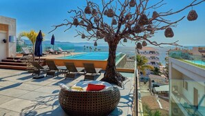 A rooftop pool area with lounge chairs, a decorative tree, and a clear view of the ocean and cityscape. - 1 BR Condo in Romantic Zone - Amazing Rooftop Pool (Puerto Vallarta)