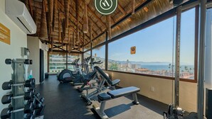 A gym with exercise equipment and a large window offering a city view. - 1 BR Condo in Romantic Zone - Amazing Rooftop Pool (Puerto Vallarta)