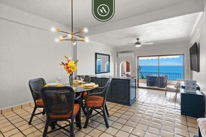 A dining area with a table and chairs, a kitchen with a view, and a balcony with a railing. - Beachfront Mexican Styled 3 BR Condo in Downtown (Puerto Vallarta)