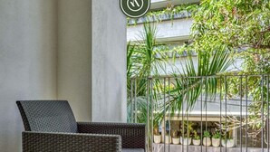 A wicker chair on a balcony with a view of potted plants and a building. - New 1 BR Condo - Oceanview Pool - 2 min to Beach (Bucerías)