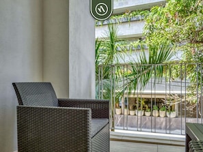 A wicker chair on a balcony with a view of potted plants and a building.