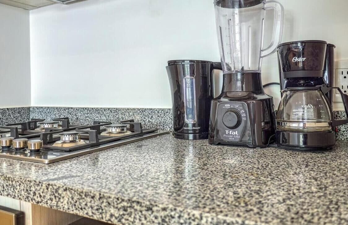 Een keuken met een gasfornuis, een blender, een koffiezetapparaat en een koffiekan.