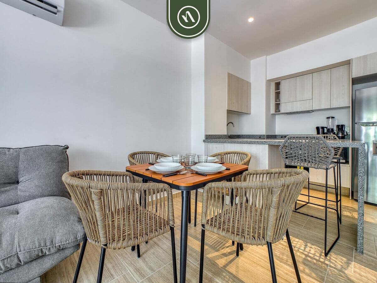A modern living space with a dining area, kitchen, and a grey sofa.