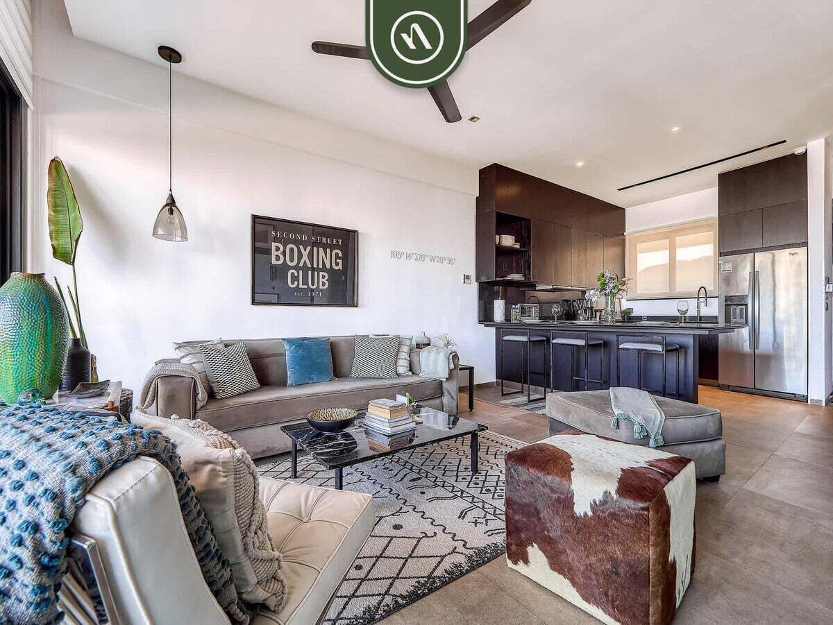 A modern living room with a sofa, coffee table, and ottoman, a kitchen with a refrigerator, and a dining area.