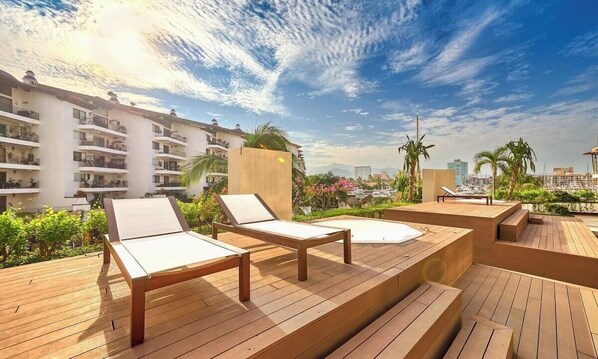 A rooftop deck with lounge chairs and a pool, overlooking a cityscape.