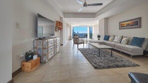 Una sala de estar moderna con sofá, mesa de centro y televisor. Hay un balcón con vistas.