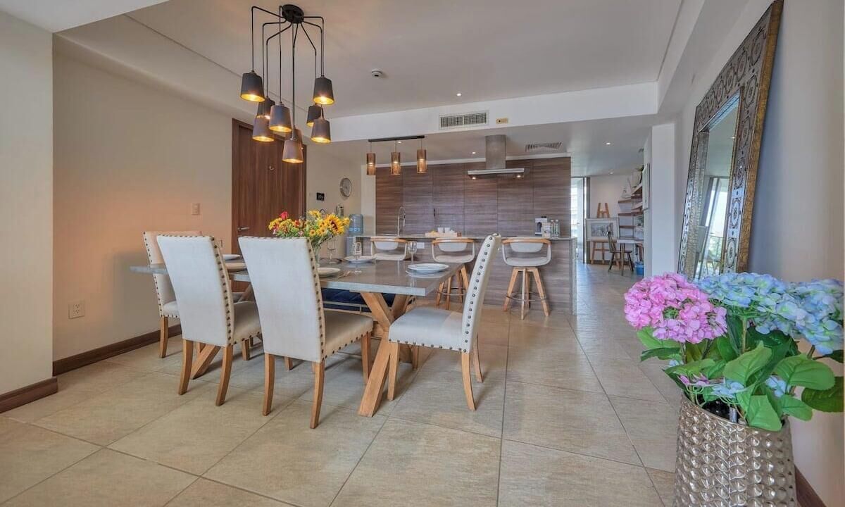 A spacious dining area with a modern chandelier, a large mirror, and a potted plant.