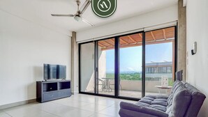 A modern living room with a sofa, a TV, and a balcony with a view.