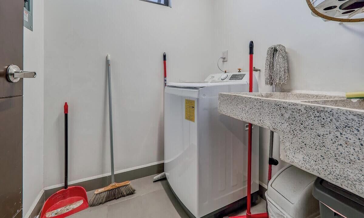 A laundry room with a washing machine, a mop, a broom, and a trash bin.