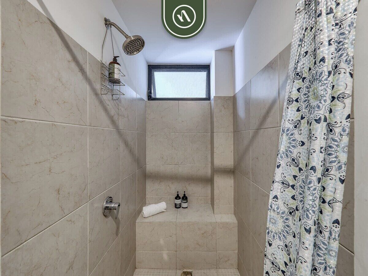 A shower with a window, a towel, and two bottles on a shelf.