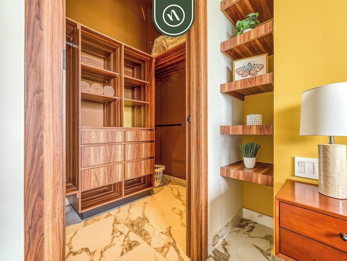 Une armoire en bois avec plusieurs compartiments, une petite plante posée sur une étagère et une lampe sur une table de chevet.