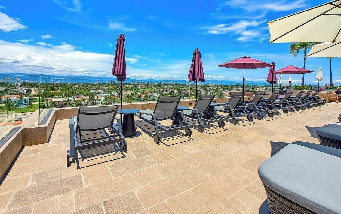 A rooftop terrace with lounge chairs and umbrellas, offering a view of a cityscape.