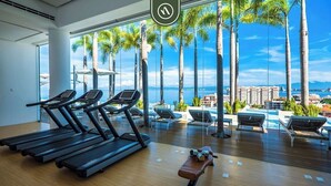 Ein Fitnessraum mit Laufbändern und einer Bank, mit Blick auf einen Pool mit Liegestühlen und Palmen.