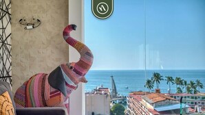 Ein Zimmer mit Meerblick, ein farbenfroher Webstuhl-Sessel und ein Sofa mit Kissen.
