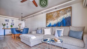 A modern living room with a grey sofa, a glass coffee table, and a dining area with blue chairs. - 3BR Condo With Private Balcony - Pool - Marina` (Puerto Vallarta)