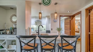 A modern kitchen with a marble countertop, three black chairs with woven seats, pendant lights, and a view into the dining area. - 3BR Condo With Private Balcony - Pool - Marina` (Puerto Vallarta)