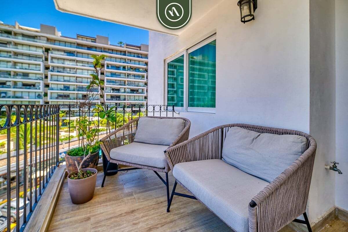 A balcony with wicker furniture, potted plants, and a view of a high-rise building.