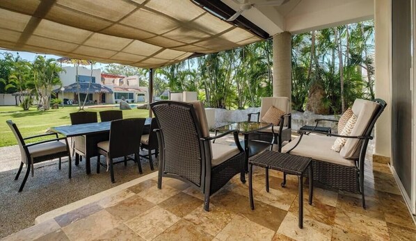 An outdoor patio with wicker furniture, a glass table, and a view of a pool and greenery. - Amazing House -private Pool - Tennis - Paddle Cour (Acapulco)