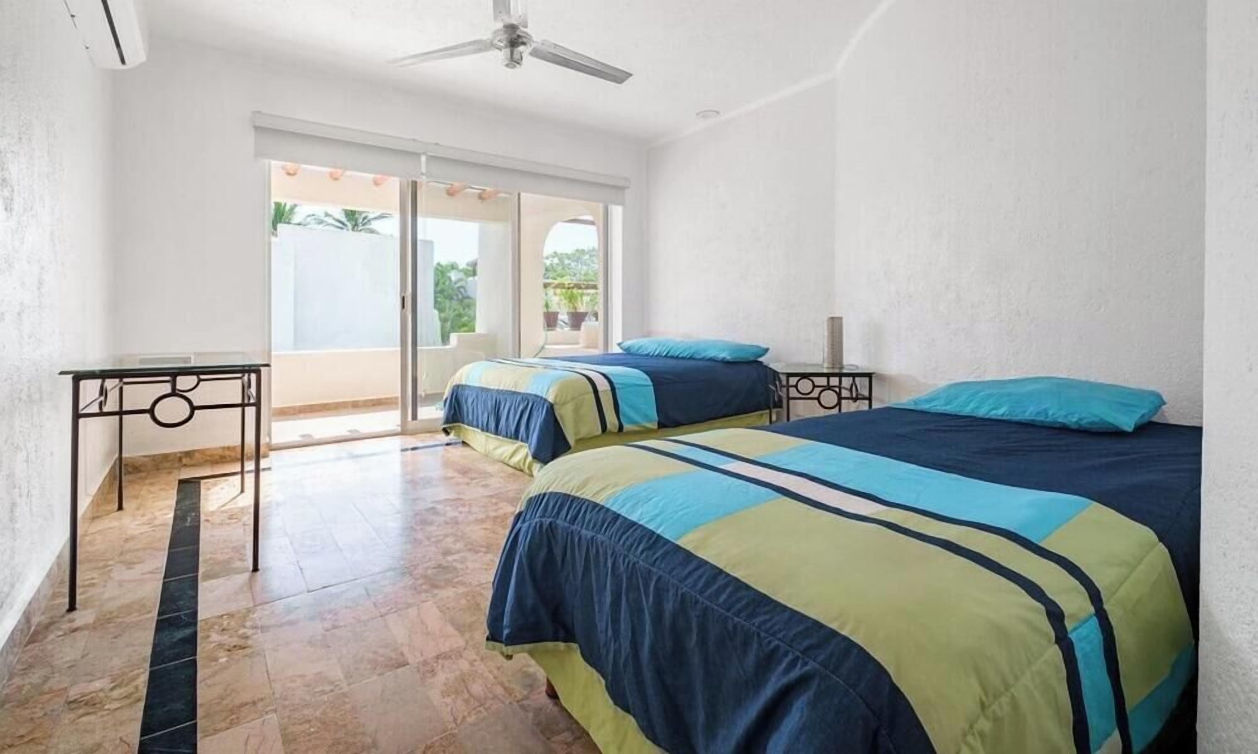 A hotel room with two beds, a ceiling fan, and a balcony with a view.