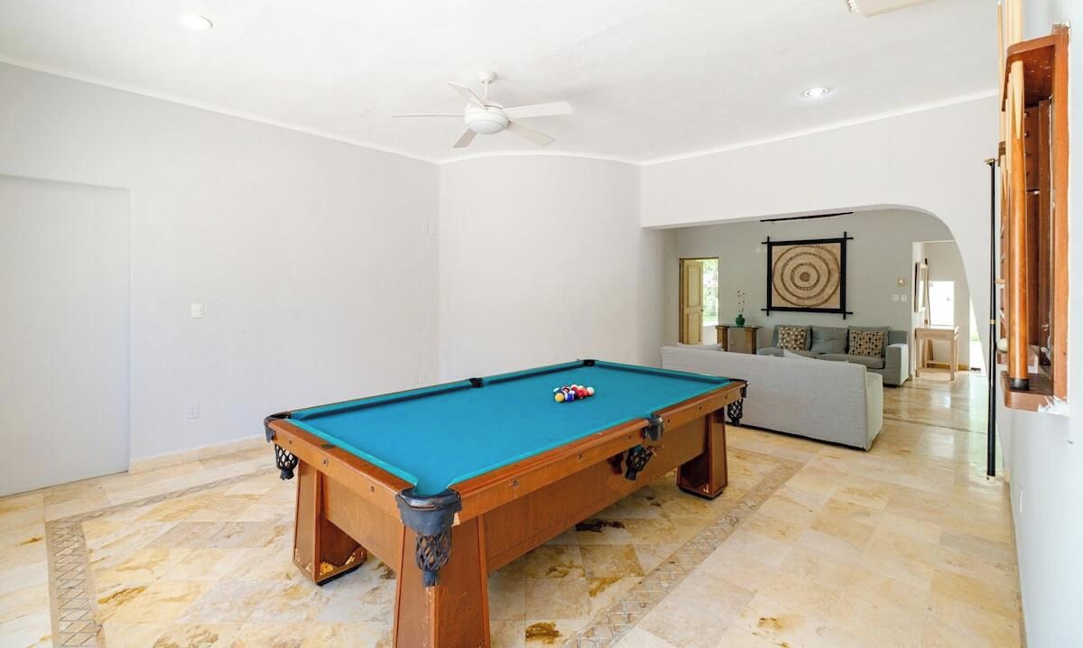 Une table de billard dans une pièce dotée d’un ventilateur de plafond, d’un canapé et d’une œuvre d’art encadrée accrochée au mur.