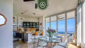 Una cucina moderna con zona pranzo dotata di tavolo e sedie in vetro, vista sull'oceano e ventilatore a soffitto.