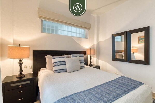 Une chambre à coucher bien rangée, avec un lit, deux tables de chevet, une fenêtre et un miroir.