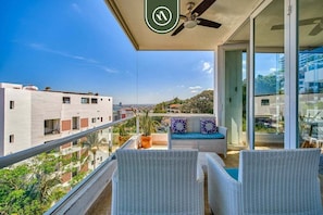 Un balcón con mobiliario de mimbre, un ventilador de techo y vista a la ciudad.