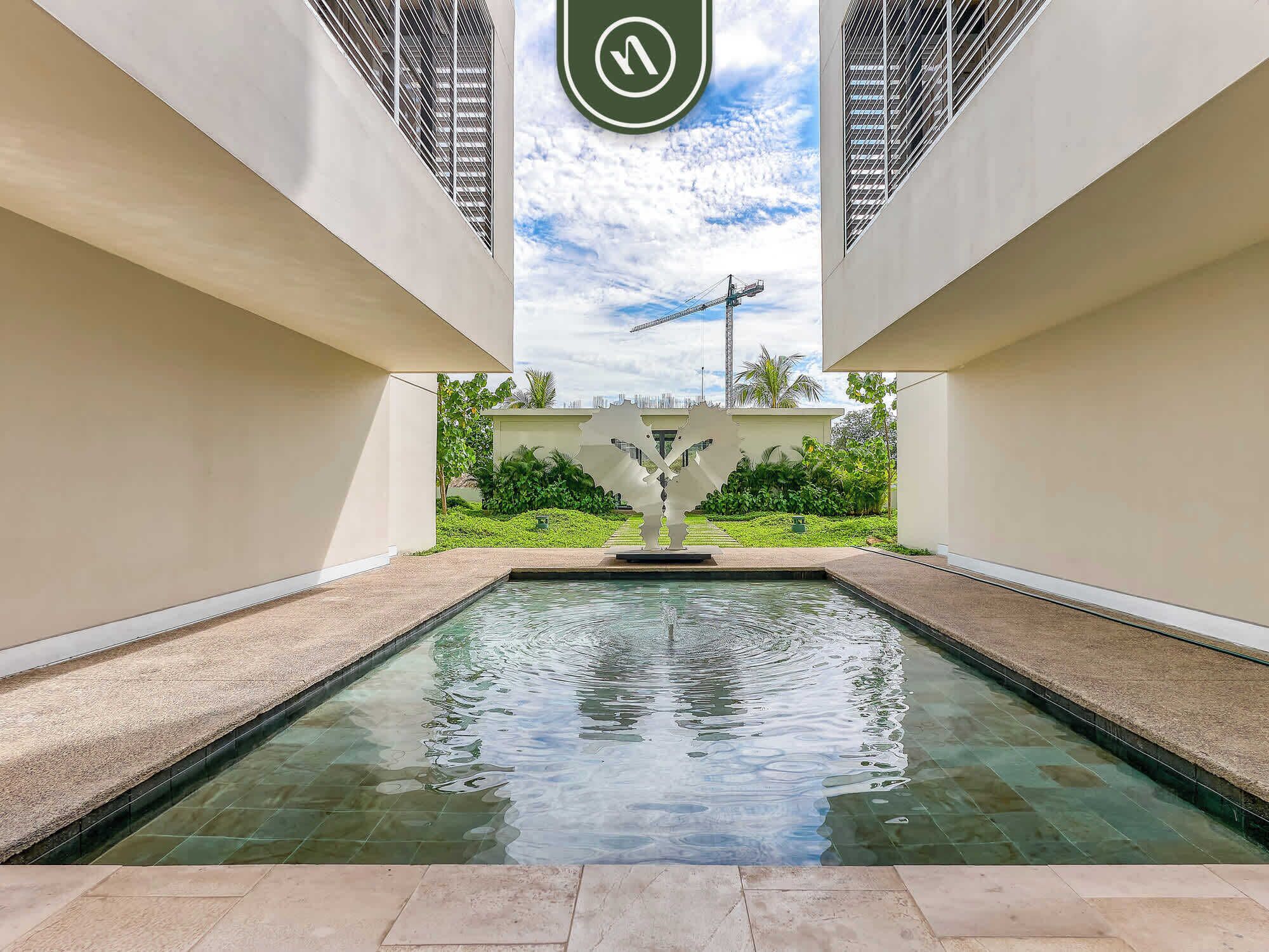 A modern building with a central pool, surrounded by greenery and a clear sky.
