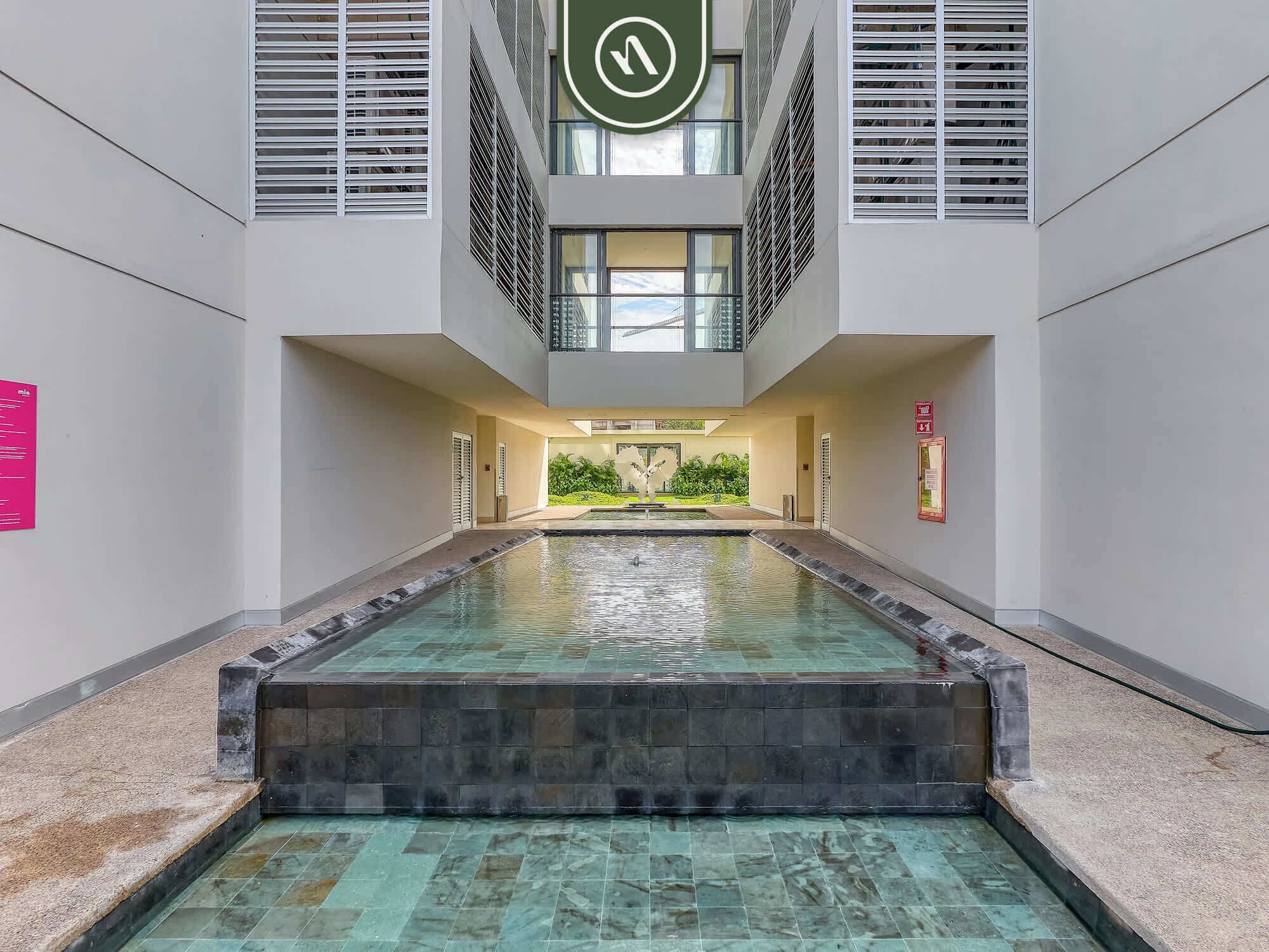 A modern indoor swimming pool with a clear view of the surrounding architecture, including a central atrium and a staircase leading to an upper level.