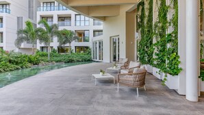 Un área de piscina interior moderna con suelo de hormigón, mobiliario de mimbre y abundante vegetación.
