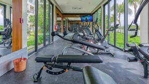 Un gimnasio con equipo de ejercicio, ventanas amplias y un extintor.