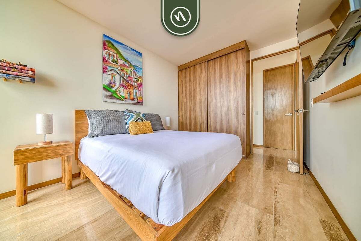 Een slaapkamer met een bed, een houten nachtkastje, een nachtkastje, een schilderij, een kledingkast en een deur.