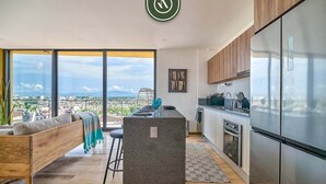 A modern kitchen with a large island, stainless steel appliances, and a view of the city. - Brand New 2BR APT - Stunning Ocean & Sunset Views (Puerto Vallarta)