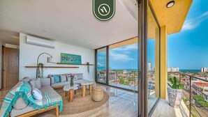 A modern living room with a sofa, coffee table, and a view of the city. - Brand New 2BR APT - Stunning Ocean & Sunset Views (Puerto Vallarta)