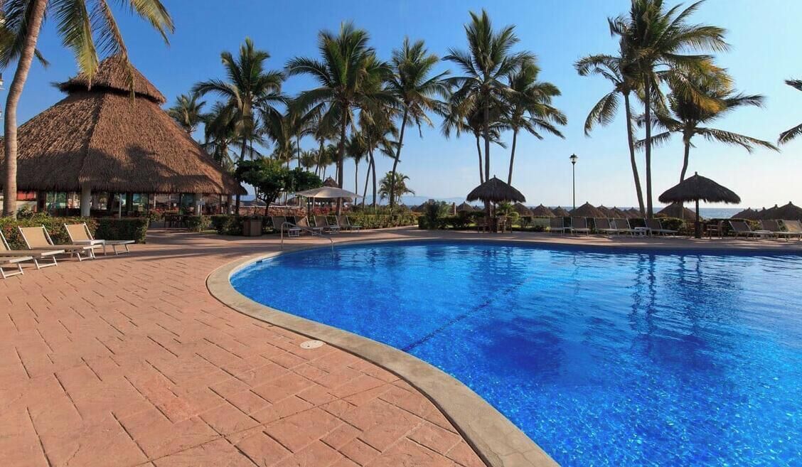A swimming pool with lounge chairs and palm trees.