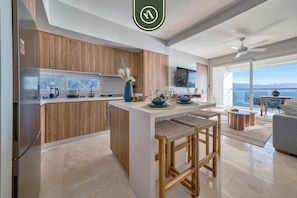 Una cocina moderna con armarios de madera, una isla central, taburetes de bar y un comedor con vistas.