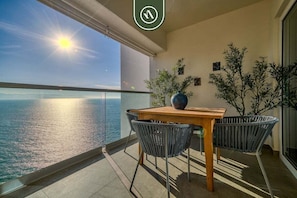 Un balcón con una mesa y sillas de madera, plantas en macetas y vistas al mar.