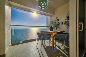 A balcony with a view of the sea, a wooden table, two chairs, and a potted plant.