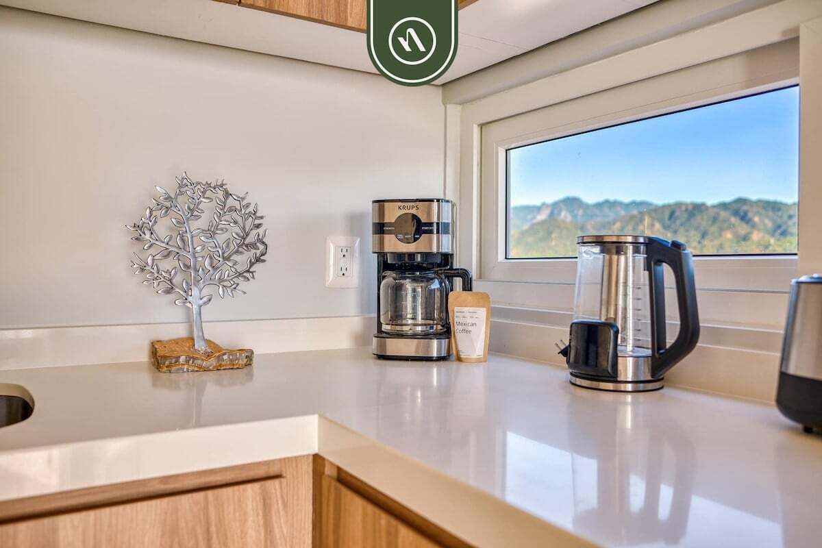 Una cocina con cafetera, hervidor y un árbol decorativo sobre la encimera.