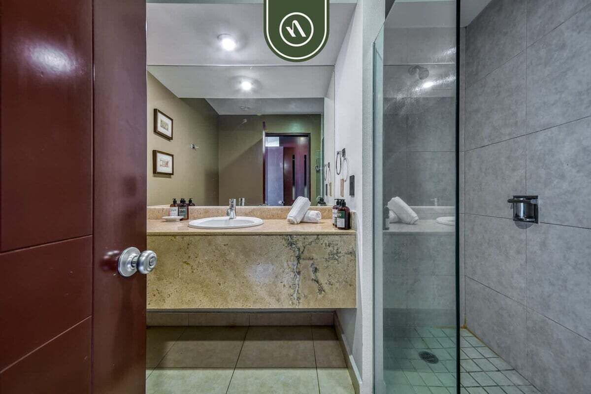 A modern bathroom with a marble sink, a glass shower enclosure, and a visible door handle.