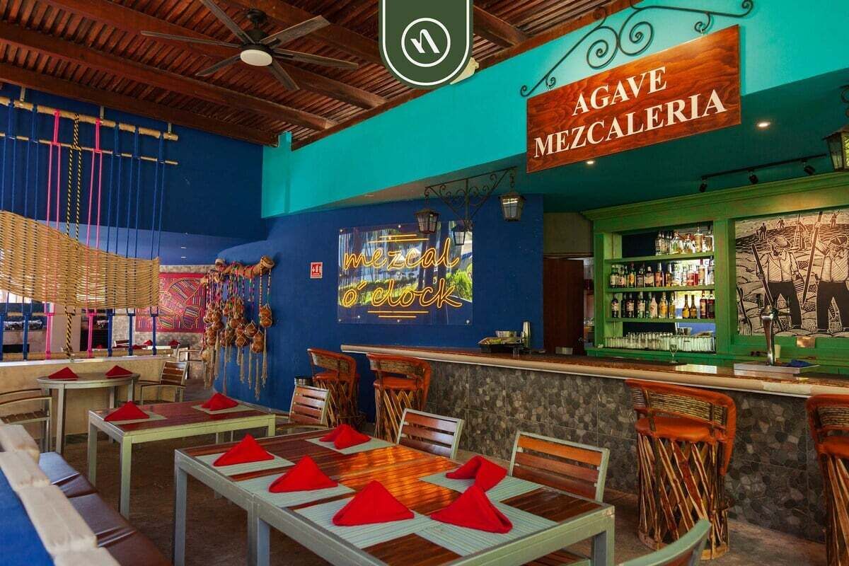 Interior de restaurante con barra, techo de madera y mesas con servilletas rojas.