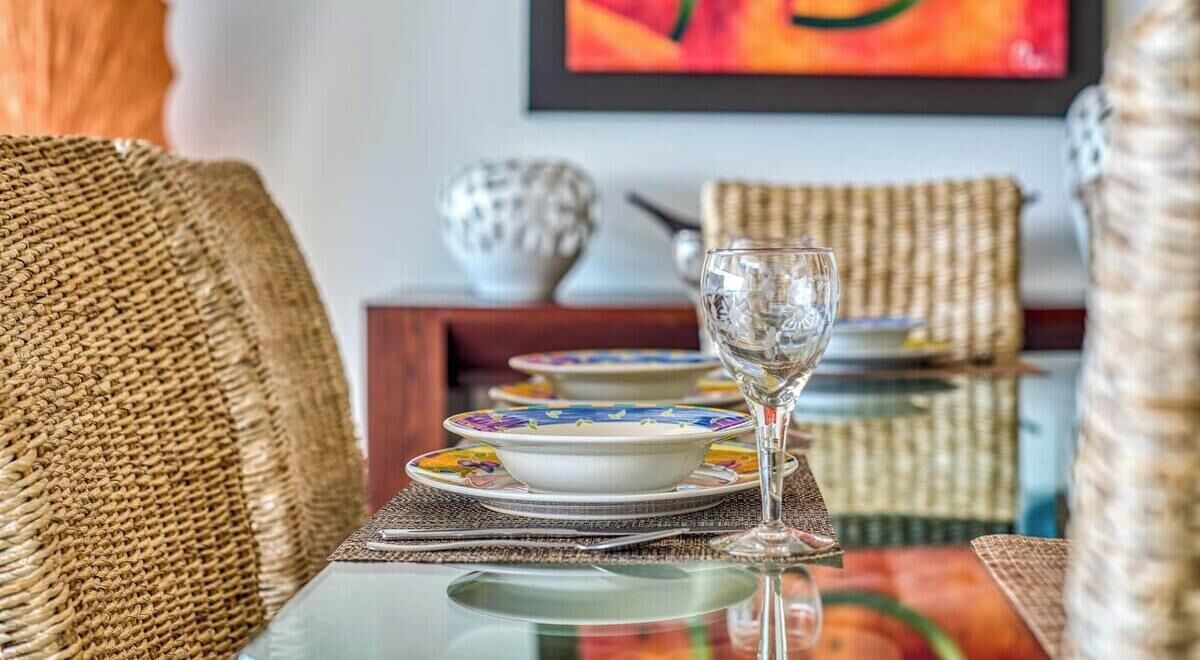 A dining area with wicker furniture, a glass table, and a colorful tablecloth.