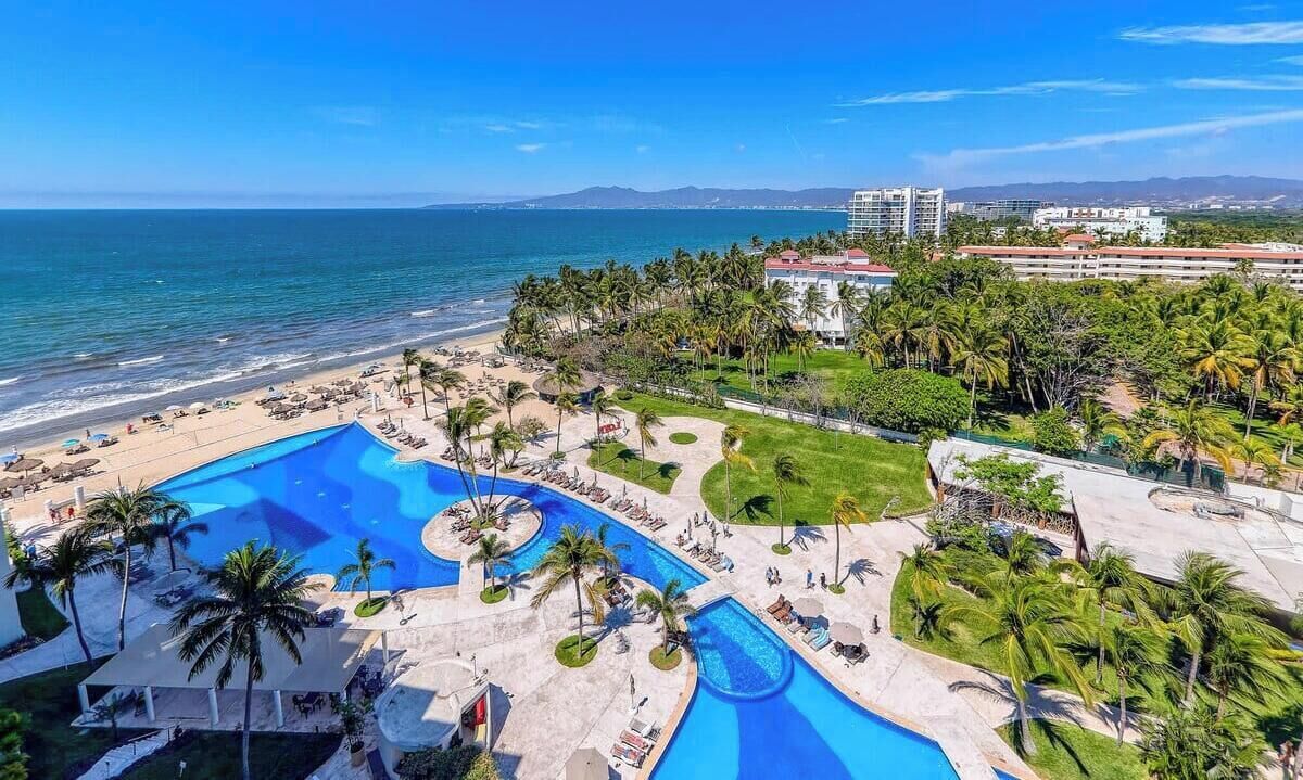 Ein Resort mit großem Pool, Palmen und einem Strand.