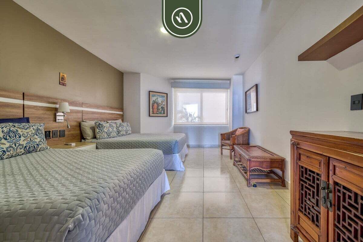 Habitación de hotel con dos camas, un armario de madera, una mesita y una ventana con vistas.