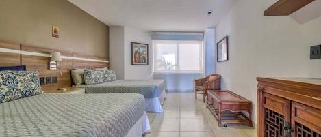 Habitación de hotel con dos camas, un armario de madera, una mesita y una ventana con vistas.