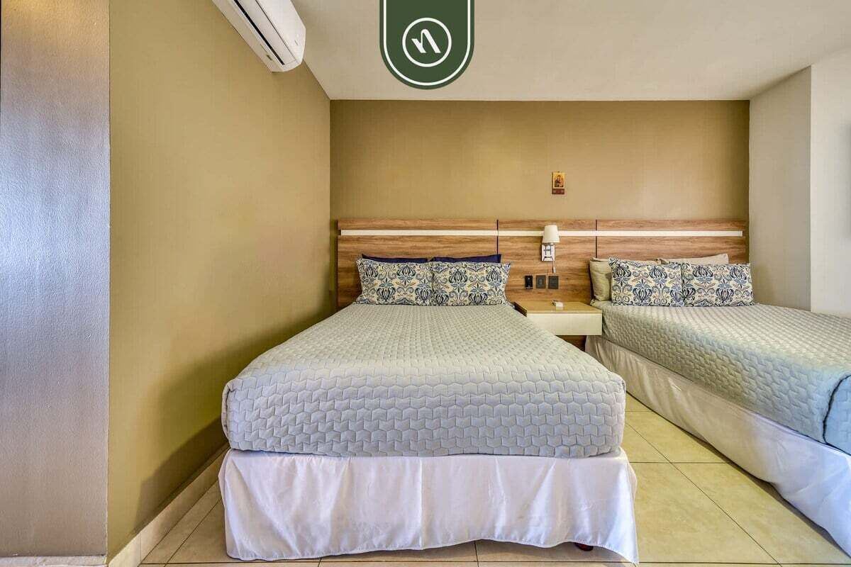 A hotel room with two beds, a wooden headboard, a nightstand, and a wall-mounted air conditioning unit.