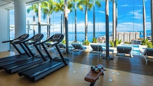 Un gimnasio con cintas de correr y sillones de descanso con vistas a una piscina y palmeras.
