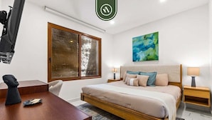 A modern bedroom with a large bed, two bedside tables with lamps, a desk with a chair, a large window with a view, and a painting on the wall. - New 1 BR Condo - Rooftop Pool - Romantic Zone (Puerto Vallarta)